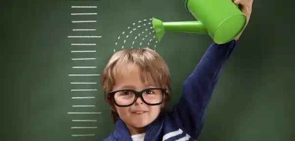 پسر بچه ای که عینک دارد و دارد با آب پاش روی کله اش آب می ریزد.